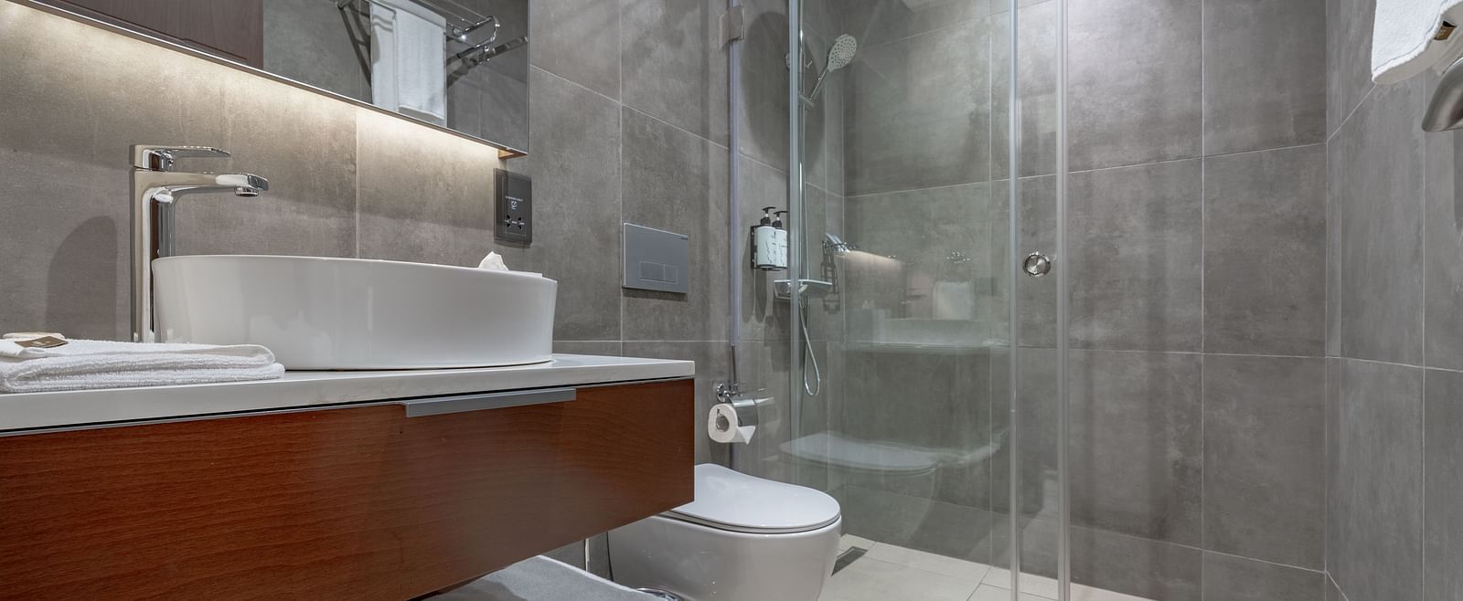 Modern Standard Room bathroom with glass shower, vessel sink, wooden vanity, soft lighting, and sleek fixtures. - The Pelican Hotel, Accra