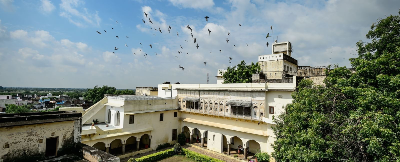 A bird's-eye view of Fort Barli reveals its courtyard, white buildings, and surrounding landscape under a partly cloudy sky.