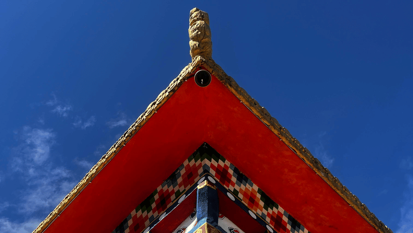 A low-angle view of a traditional pagoda-style roof with vibrant red, blue, and gold patterns against a clear sky.