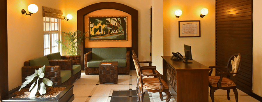 Reception lobby at The Richmond Puducherry featuring a desk with chairs, and a seating area with sofa set and a centre table.