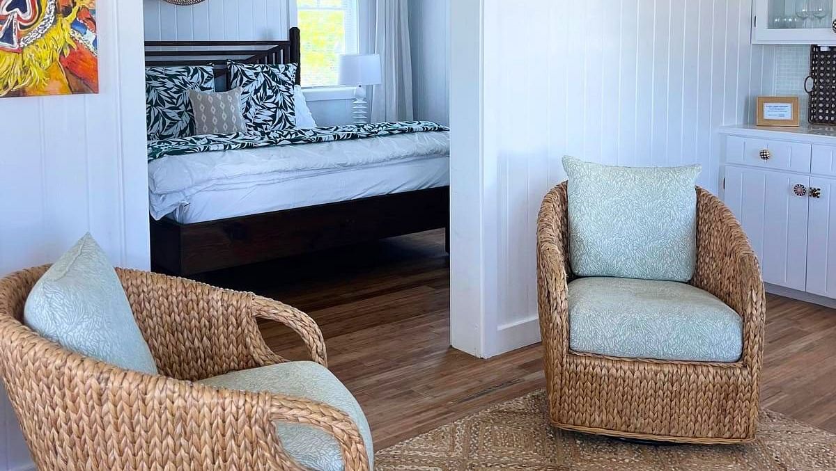 An interior view of a room with tiled floors. Two wicker chairs and a small table are in the foreground, with a glimpse into another room with a mirror and artwork on the wall | Abaco Inn