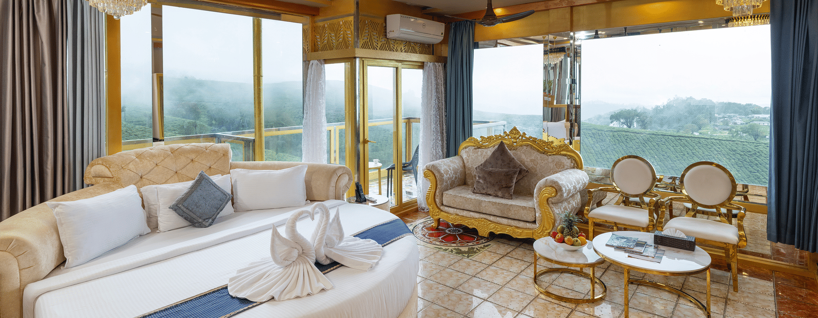 A wide-view of the Jacuzzi 180-degree Suite bedroom at Parakkat Nature Hotel and Resorts, Munnar, featuring decorative chairs and a sofa, patterned floor tiles, and large windows providing a view of outdoors.