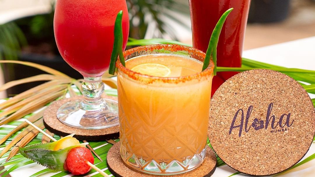 Three tropical cocktails with garnishes and an Aloha coaster at Hotel Mumbai House Mindspace, Malad.