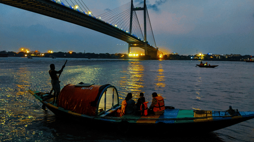 a boat with people on it travelling on a waterbody in front of the howrah bridge in Kolkata.