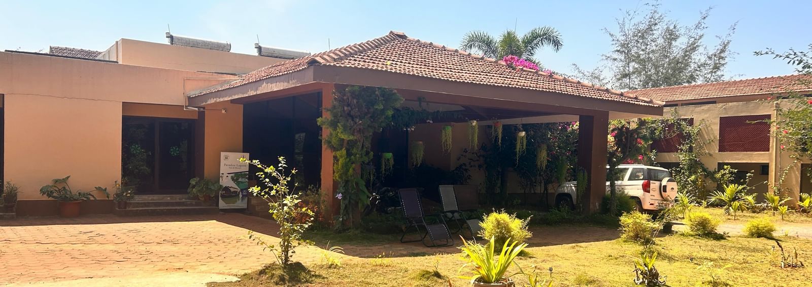The beautiful Paradise Wild Hills Resort, Kollur, with a covered porch and surrounding green lawns and plants.