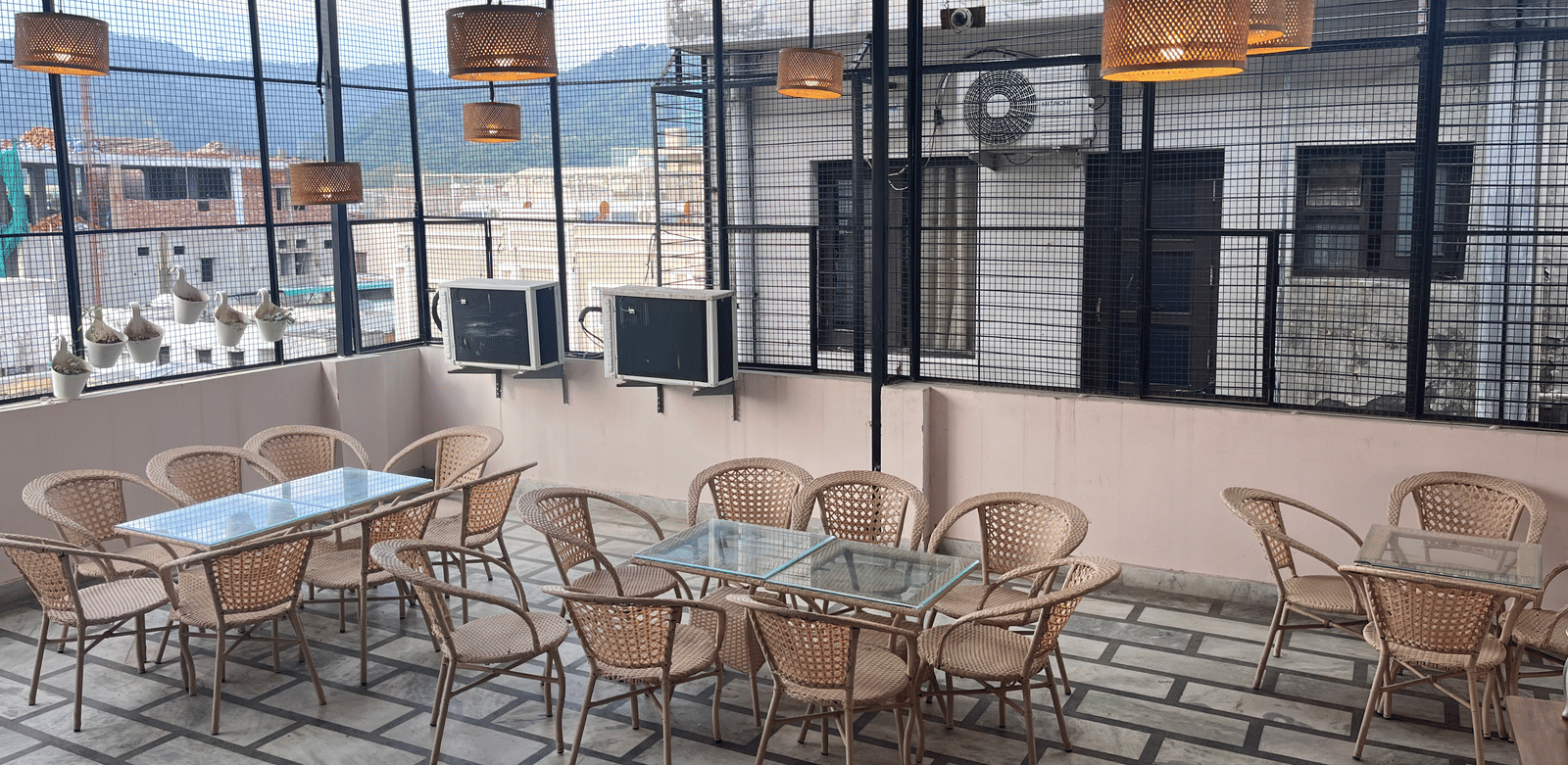 Full view of the rooftop restaurant at Perfectstayz Value Dhruv Nanda, Haridwar, with warm lights hanging from the tin ceiling along with a beautiful mountains in the background.