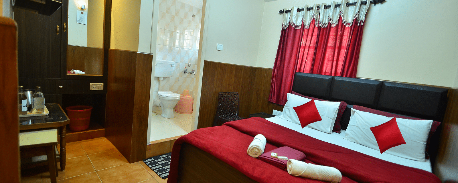 Image of a room with a large bed and a washroom in the corner at BN Tourist Home, Ooty.