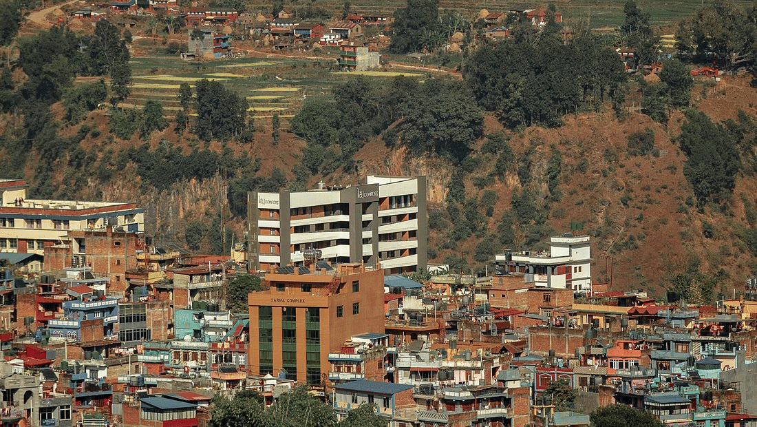Hillside townscape with terraced fields rising behind closely packed houses and the hotel building visible at the centre at Ila Comfort, Baglung.