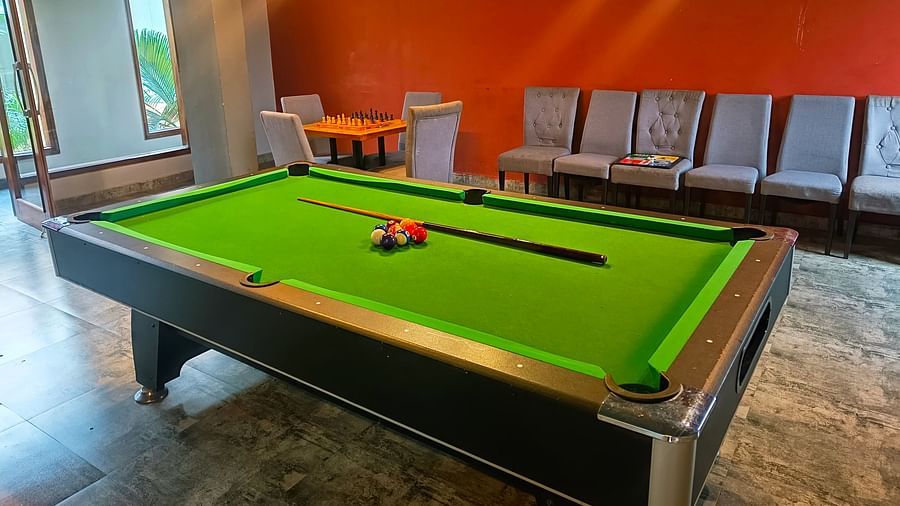 A side view of the pool table with a cue stick and a ball placed in the centre, with chairs adjacent to the wall at DLS Forest Vines Resort & Spa, Ramnagar (Jim Corbett).