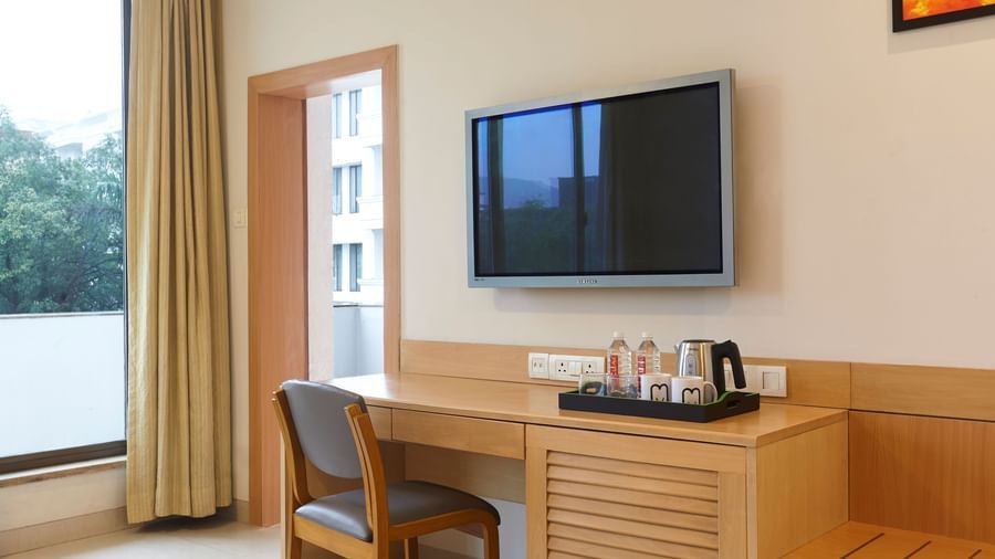 A close-up of a hotel room desk and TV at Monday Hotels Mahape, Navi Mumbai, with a view of a window.