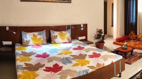 A spacious bedroom with a double bed, colourful bedding, a sofa set and a wall painting above the bed at Jaypore360 Homestay - Best Homestays in Jaipur.
