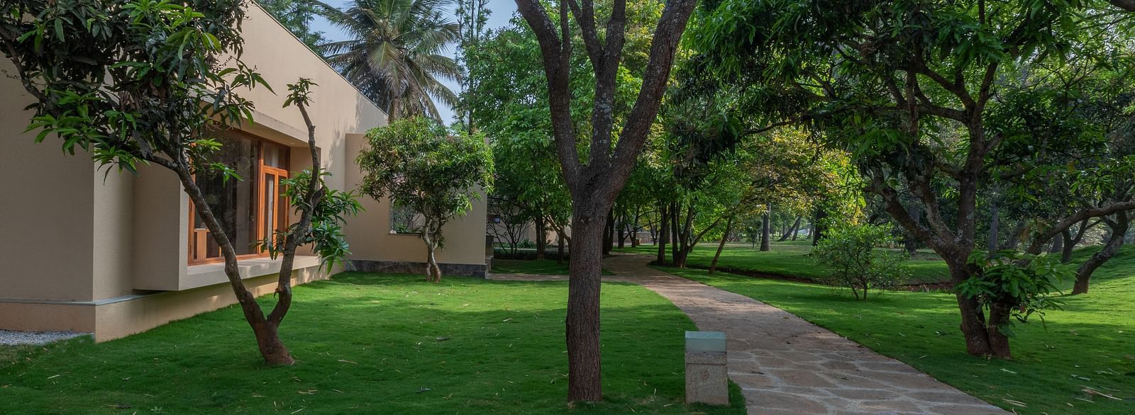 Garden path with trees and grass, building in background, outdoor landscape, natural setting - Shreyas Retreat