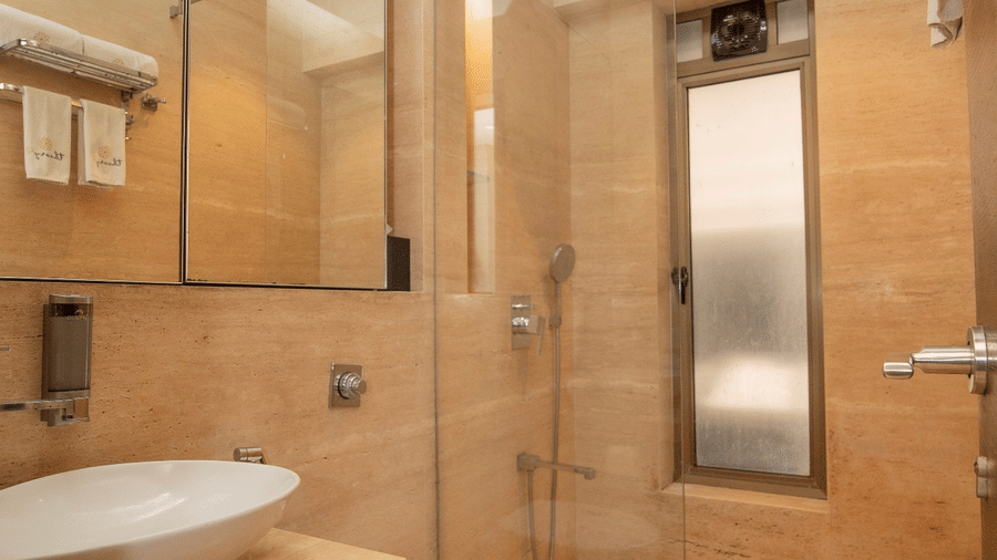 Bright tan-tiled bathroom at Theory9 - Premium Serviced Apts, Khar, with a white vessel sink, toilet, and glass shower partition.