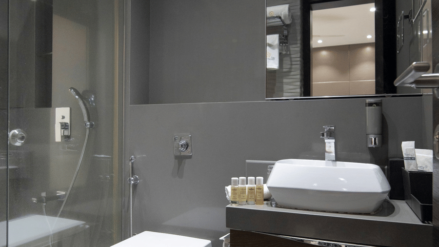 Modern grey-tiled bathroom at Theory9 - Premium Serviced Apts, Khar, featuring a vessel sink and glass-enclosed walk-in shower.