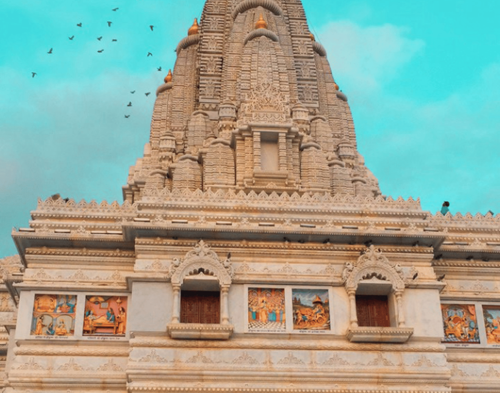 Top spire (Shikhara) of a temple with a vibrant turquoise sky background and tiny birds circling the mast.