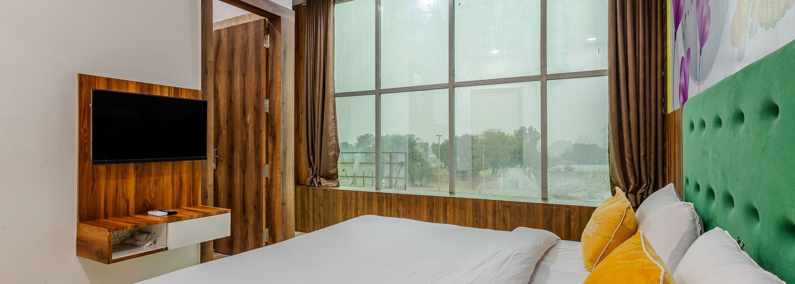 A bedroom with large windows, yellow cushions, and minimal wooden furnishings - Lime Tree Hotels & Banquet, Vrindavan