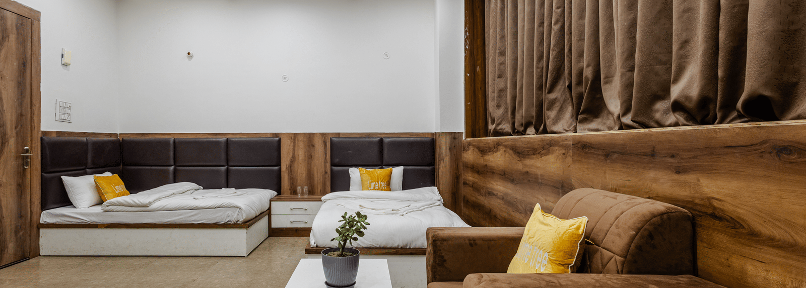 A living area with a wooden sofa set, white table, and beige curtains on the window - Lime Tree Hotels & Banquet, Vrindavan
