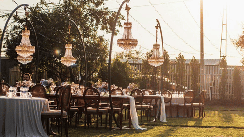 A banquet arrangement in an open garden with over head chandeliers. 