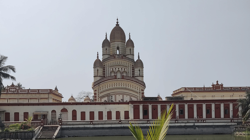 A far out view of a temple which houses Goddess Kali of Dakshineswar with a waterbody in the foreground.