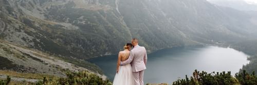 A wedding couple hugging each other on top of a mountain overlooking a lake by the valley.