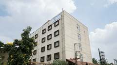 A low-angle shot of the VITS Select, Bengaluru exterior, with square windows and lush tree foliage against a cloudy backdrop.