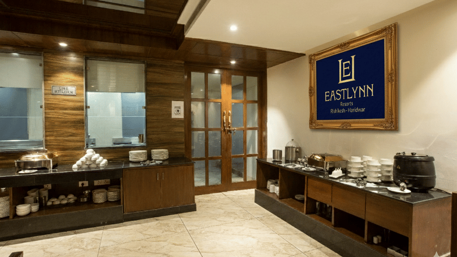 The hotel's dining area featuring a clean, organised buffet counter with hot dishes and the Eastlynn logo displayed — Eastlynn Resort, Rishikesh