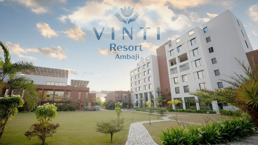 An expansive manicured lawn and curved pathway lead toward the stylish buildings of Vinti Resort, Ambaji at sunset.