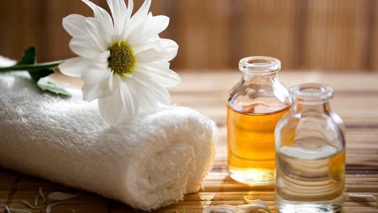 an image showing two different massage oils kept in a glass bottle with a towel next to it and a rose on top of it - Panchakarma Treatment Bangalore