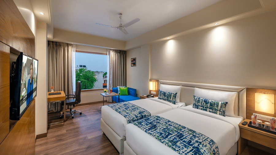 Spacious club room with twin beds, seating area, and large window with a TV