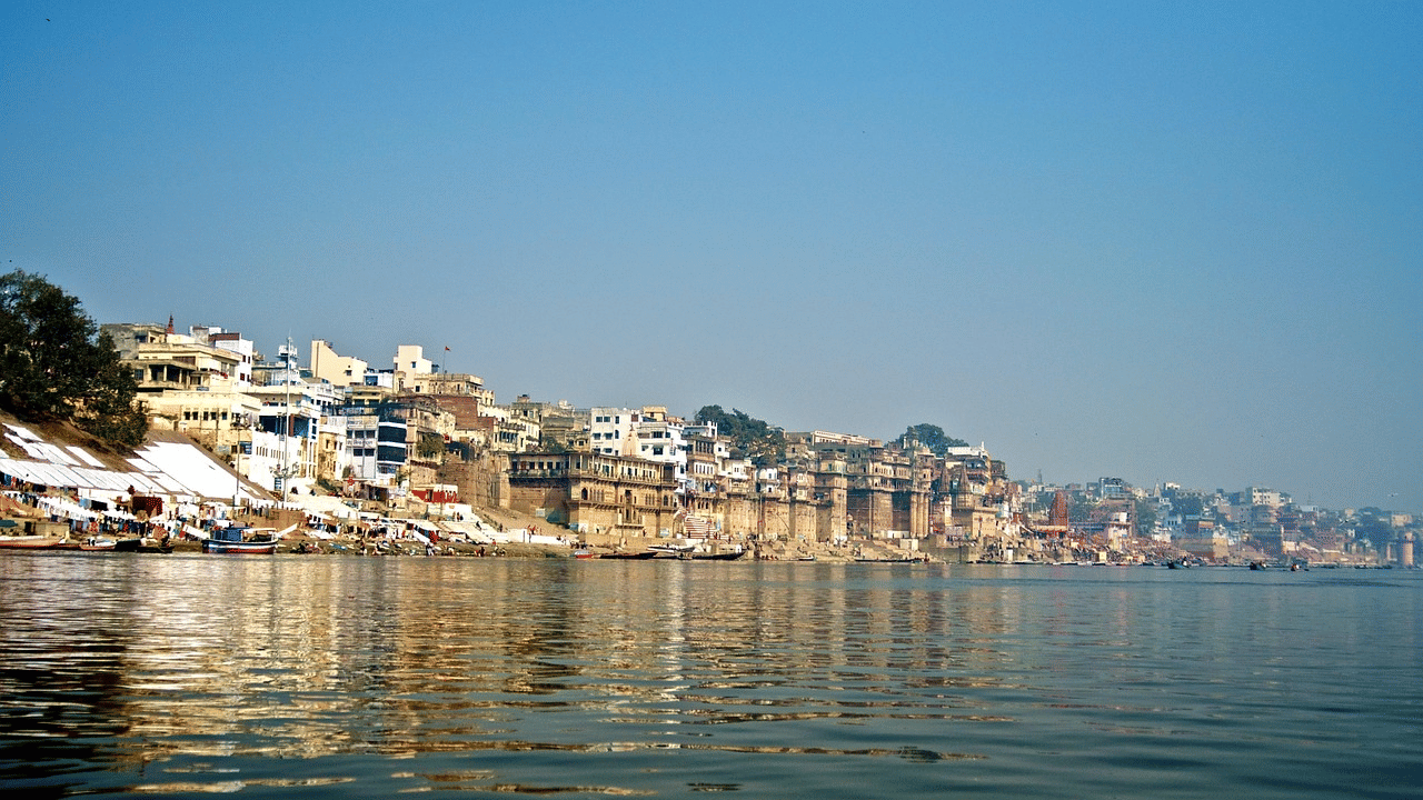 A riverbank featuring buildings under a clear blue sky, with reflections of the buildings in the water.