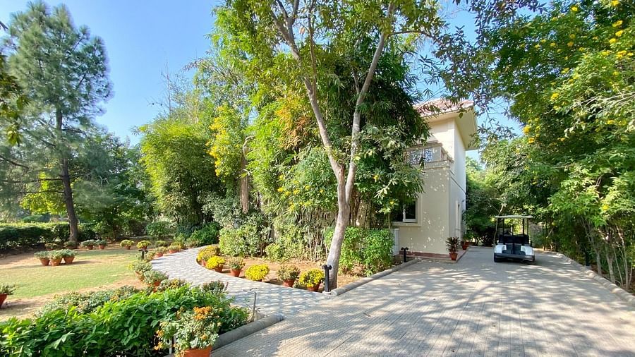 A huge house with green trees and lawn inside the compound, pictured with a golf cart parked on the front of the house - Karma Lakelands.