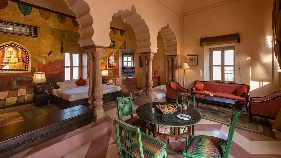A suite at Neemrana's Tijara Fort Palace features a bedroom with painted walls and a living area with colorful furniture and arched doorways.