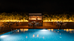A tranquil nighttime view of the hotel's outdoor swimming pool, lit up with glowing lights, with a seating area surrounded by plants at The Residency Towers Rameswaram.