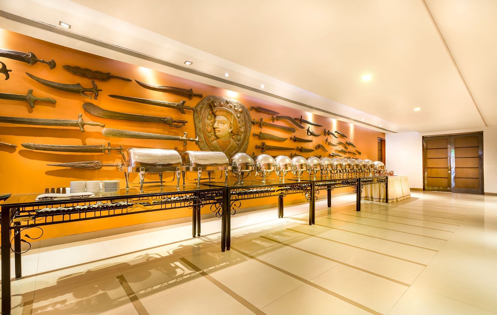 Hotel   with a long buffet table, ornate wall decor featuring swords and shields, and warm lighting.