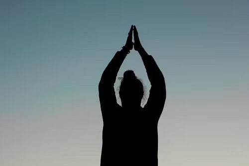 Silhouette of a person performing a standing yoga pose at sunset.