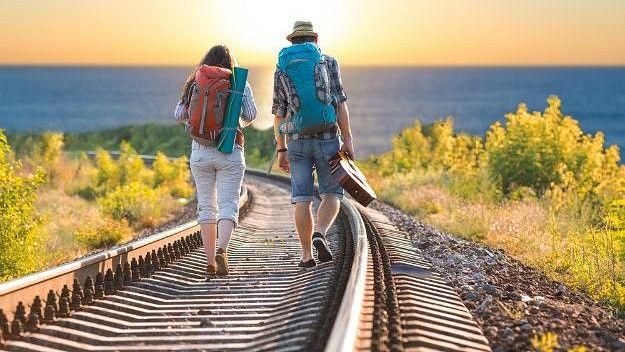 Two travellers walking on a railway line with the sun in front of them