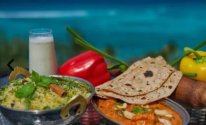 2 bowls of curry with flatbread (roti), vegetables, and a glass of buttermilk, blurred ocean in background | A Stone's Throw Away