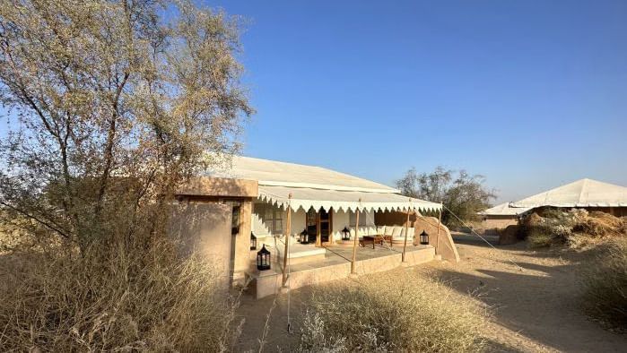 A luxury desert tent with an extended canopy stands amid a dry landscape with sparse trees, under a clear sky - MANVAR Resort & Desert Camp