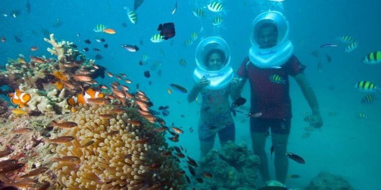 Two people sea walking among tropical fish and coral.