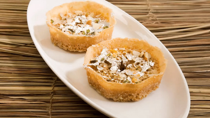 Top side angle view of delicious Shahi Ghewar served on an oval-shaped plate, garnished with dry fruits.