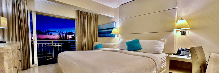 Modern hotel room with a king size bed, bedside lamps, a balcony, and a view of the evening sunset at The Soco Hotel.