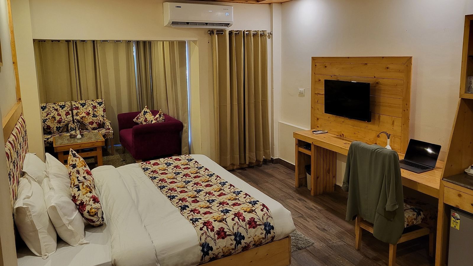 A well-lit hotel room with a bed, colourful cushions, a TV, and a work desk at Dagshai Manor Kasauli - Inde Hotels.