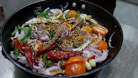 A colourful pan of fresh ingredients including onions, tomatoes, garlic, spices, and herbs being prepared near Matsya Island Retreat 