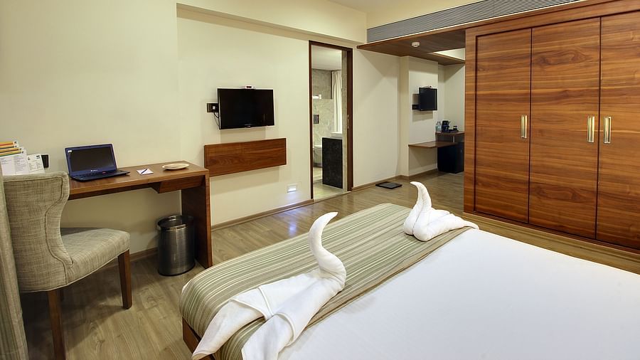 A well maintained suite room showing a study table and chair, two towel swans, a wooden wardrobe and a living rooms entrance