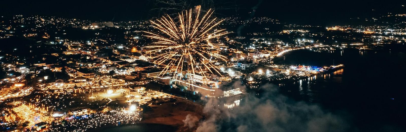 A firework bursts over a cityscape at night, illuminating the urban scene with a bright display.