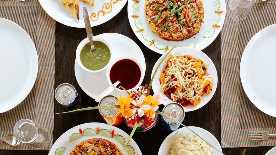 A bright overhead shot of a dark dining table set with 3 plates of food and sides, at Daksh Resort & Amusement Park, Sasan Gir.