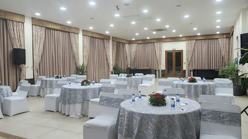 Elegant event hall with round tables covered in patterned tablecloths, white chairs, floral centerpieces, and soft overhead lighting - Suryavilas Luxury Resort and Spa