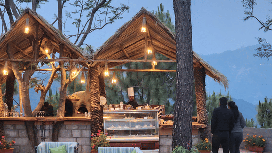 Outdoor gazebo dining setup at Suryavilas resort with warm hanging lights, a food display counter, and a couple enjoying mountain views at dusk in Kasauli