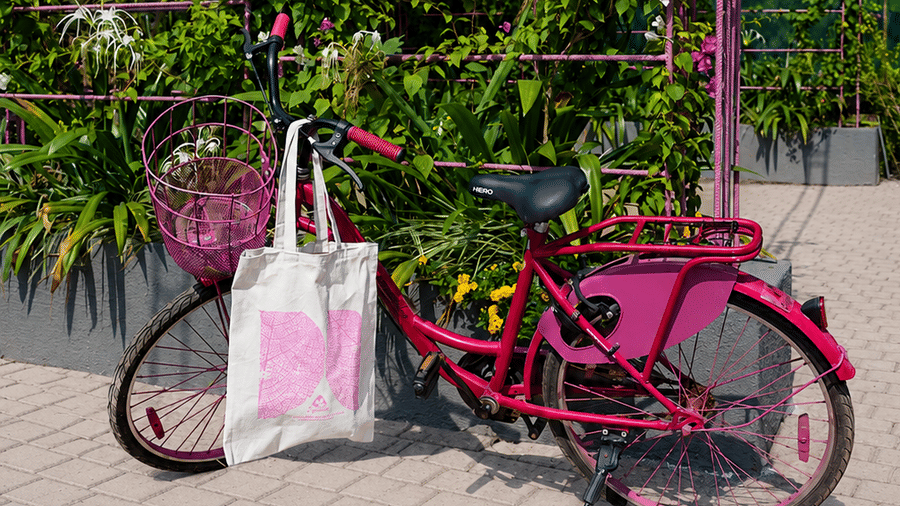 A bicycle stands with a tote bag on its basket, parked next to a floral installation, on a paved pathway at Bougainvillea, Alibaug.