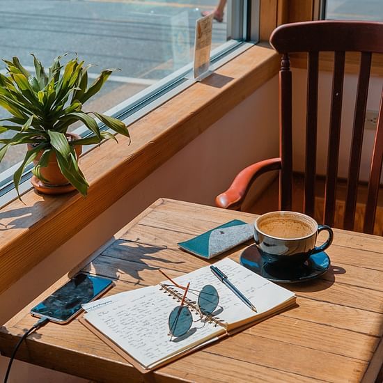 A cup of coffee a diary glasses and mobile phones on a table at a cafe
